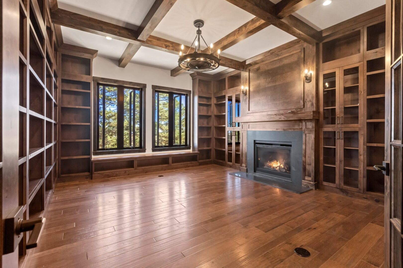 Mountain ranch custom home library study with wall to wall wood shelving, grand fireplace and candelabra chandelier