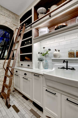 Butler's pantry with white cabinets and built-in sliding ladder and apron front sink
