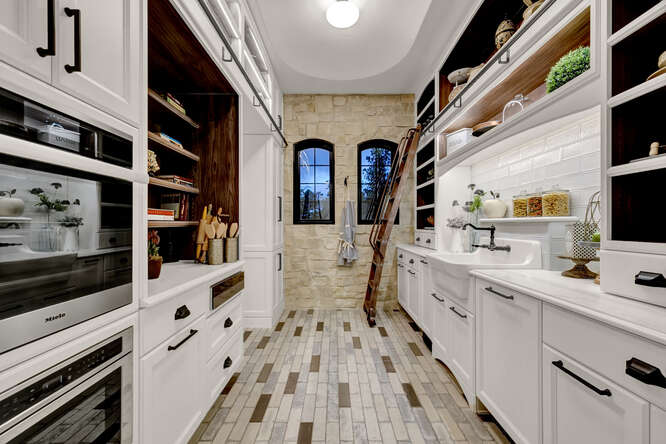 Butler's pantry with white cabinets and built-in sliding ladder and apron front sink