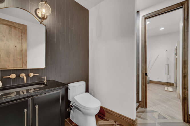 Bathroom with black vanity cabinets and brass wall mount faucets and gray wall tile