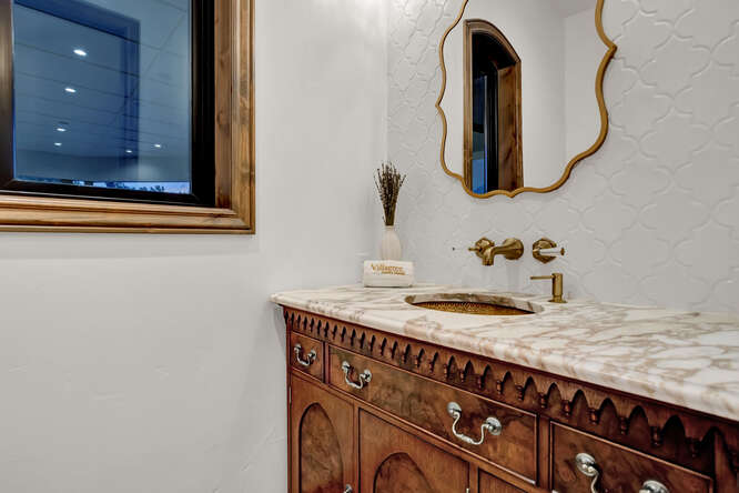 Powder bathroom with brass sink and stone top vanity cabinet