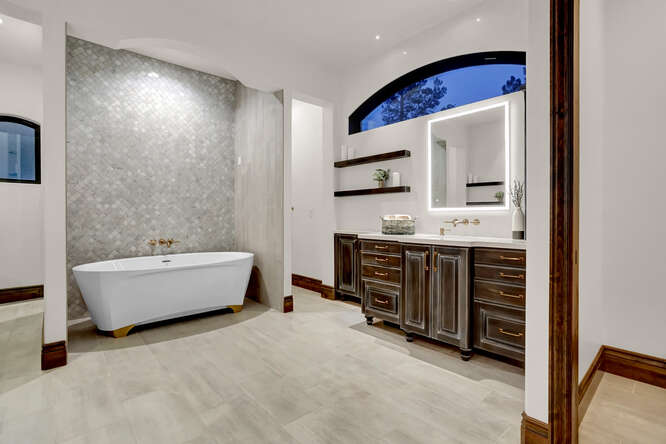 Primary Bathroom with free standing tub and full wall tile and dark tone wood cabinets