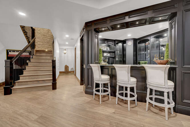 Luxury wet bar with black wood paneling with barstools